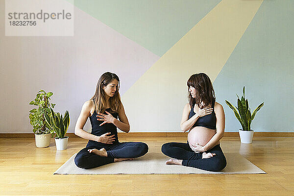 Ausbilder unterrichtet schwangere Frau  die vor der Wand im Studio sitzt  in Yoga