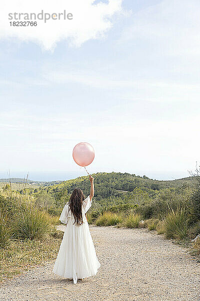 Mädchen im weißen Kleid hält einen Ballon auf dem Weg