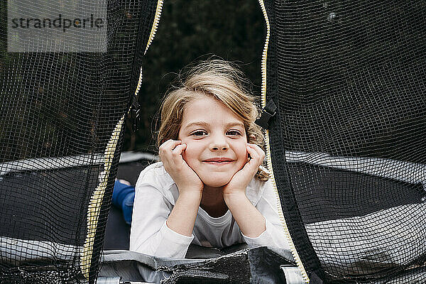 Lächelndes süßes Mädchen  das auf dem Trampolin im Garten liegt