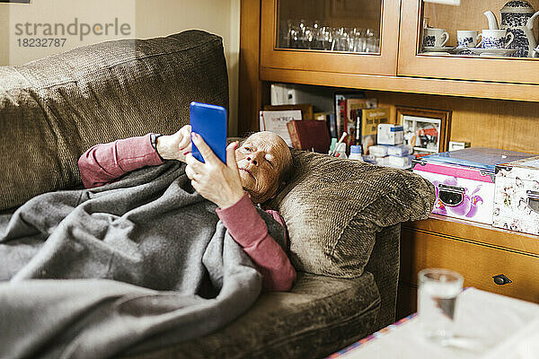 Ältere Frau benutzt Smartphone auf Sofa zu Hause