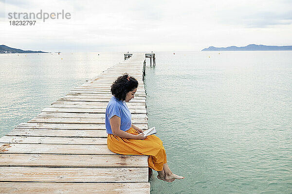Woman reading book sitting on jetty
