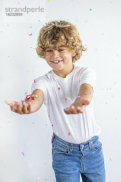 Lächelnder Junge  der mit Konfetti vor weißem Hintergrund spielt