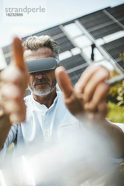 Reifer Mann gestikuliert mit VR-Brille vor Solarpaneelen