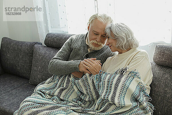 Älteres Paar kuschelt auf der Couch unter einer Decke