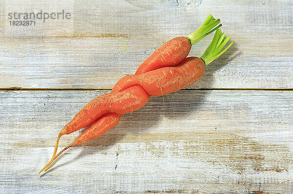 Two intertwined carrots lying on wooden surface