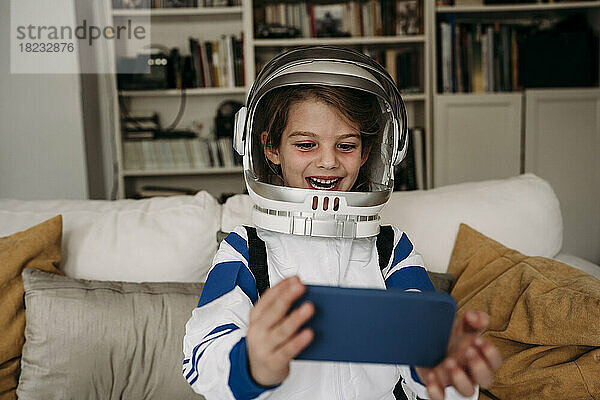 Happy girl wearing space costume having video call on mobile phone at home