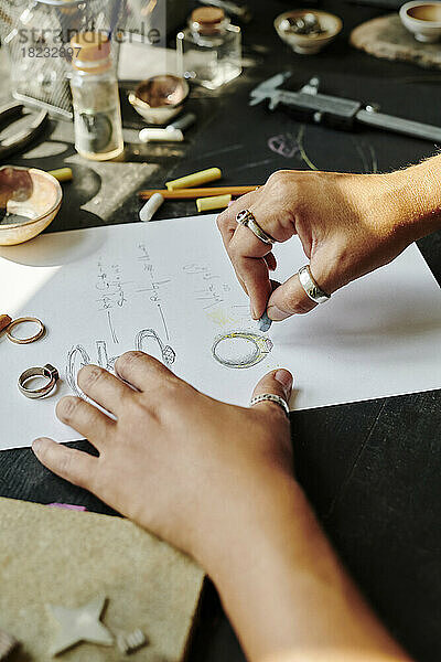 Hände eines Juweliers skizzieren Ringdesign auf Papier an der Werkbank