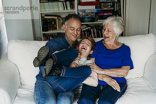 Happy girl with father and grandmother enjoying on sofa at home