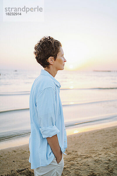 Nachdenkliche Frau steht bei Sonnenuntergang am Strand