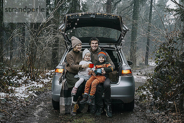 Glückliche Familie mit Kaffeetassen  die Zeit miteinander im Kofferraum eines Autos verbringt