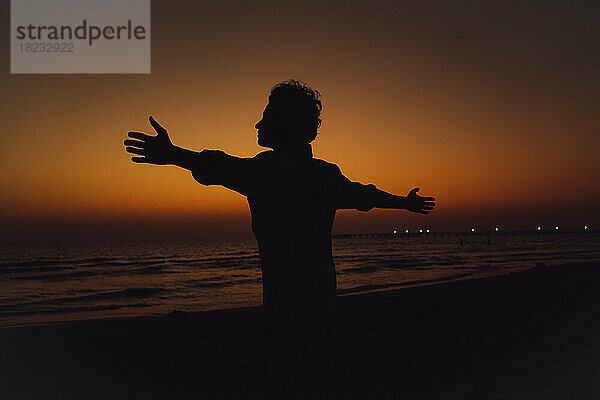 Silhouette of woman with arms outstretched standing at beach