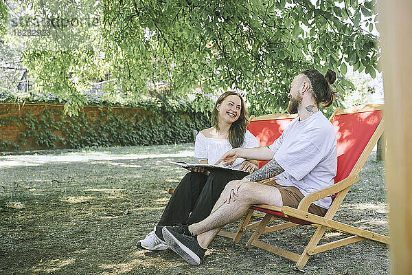 Glückliches Paar mit Buch sitzt auf Liegestühlen im Hinterhof