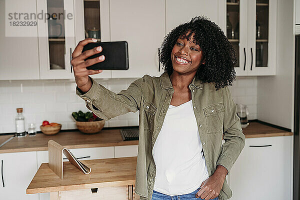 Lächelnde Frau  die zu Hause in der Küche ein Selfie mit dem Smartphone macht