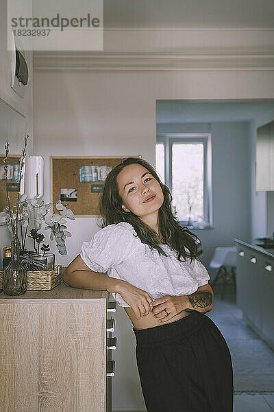 Smiling woman leaning on cabinet at home