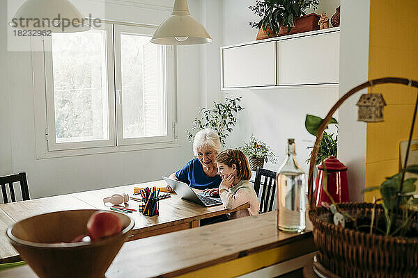 Ältere Frau hilft Enkelin beim Lernen per Laptop auf dem heimischen Tisch