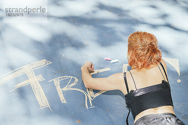 Redhead woman lying and writing with chalk on footpath