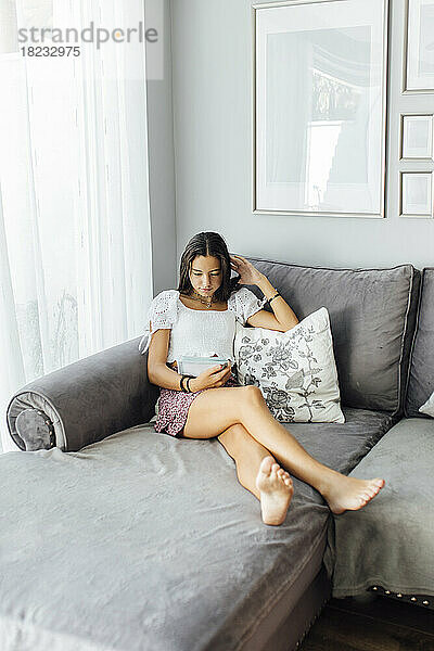 Girl reading book sitting on sofa at home