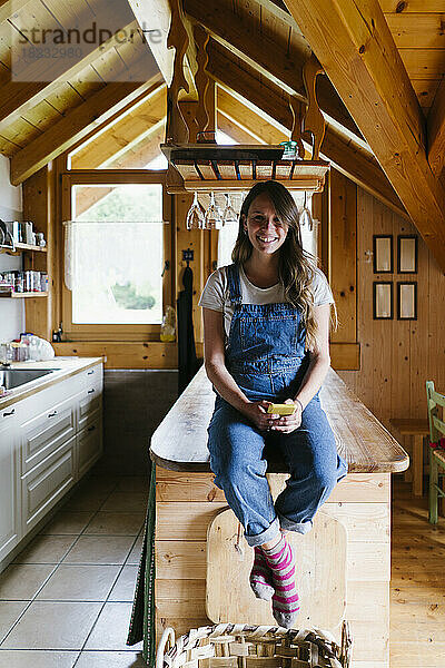Glückliche Frau mit Smartphone sitzt auf Kücheninsel