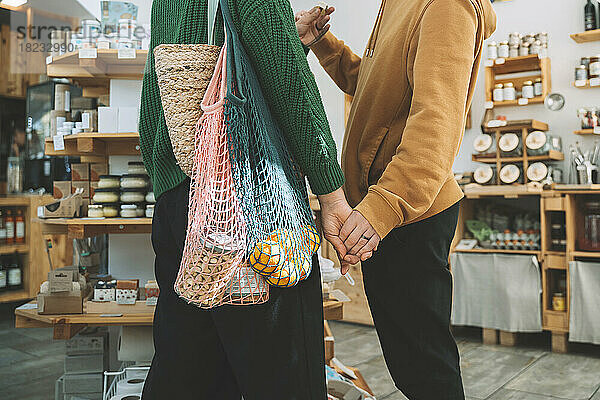 Frau mit Netzbeuteln hält Mann im Supermarkt an der Hand