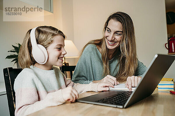 Glückliche Mutter hilft Tochter beim Lernen über Laptop auf dem Tisch