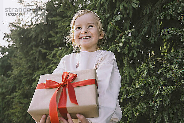 Glückliches Mädchen hält Geschenkbox in der Nähe eines Tannenbaums