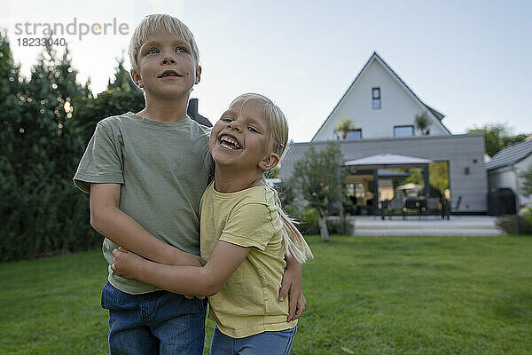 Glückliches Mädchen umarmt Bruder im Hinterhof