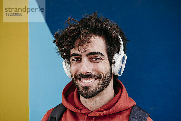 Glücklicher Mann mit kabellosen Kopfhörern vor bunter Wand