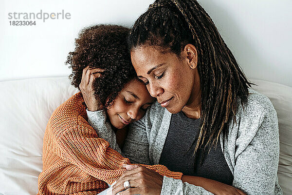 Lächelnde Frau umarmt Tochter zu Hause auf dem Sofa
