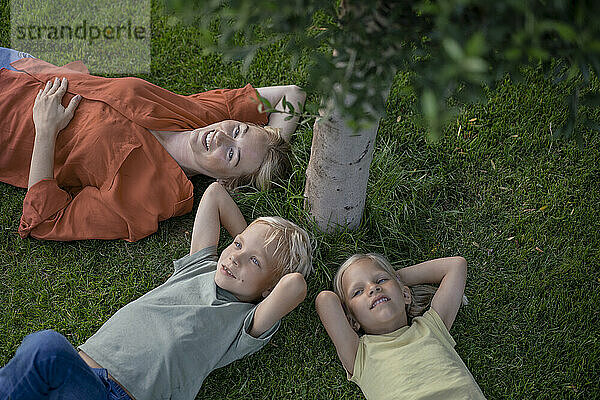 Smiling mother with children resting on grass in back yard