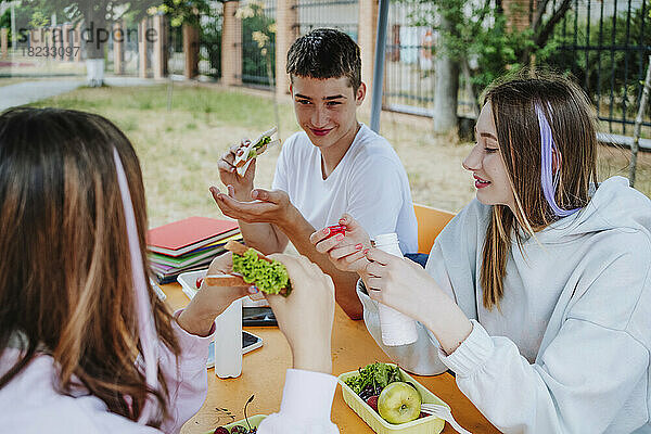 Mädchen mit Jungen essen am Tisch auf dem Schulhof zu Mittag