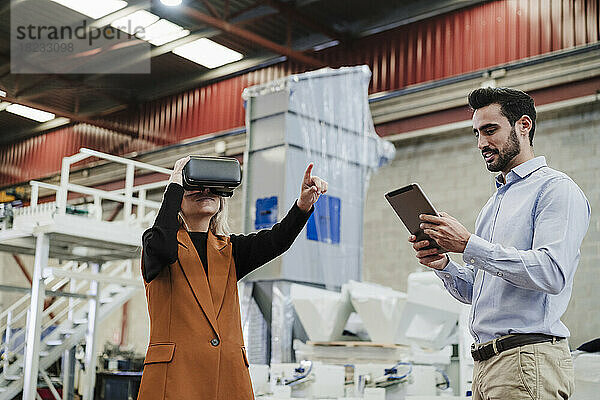 Geschäftsmann benutzt Tablet-PC  während Kollege gestikuliert  indem er einen Virtual-Reality-Simulator trägt