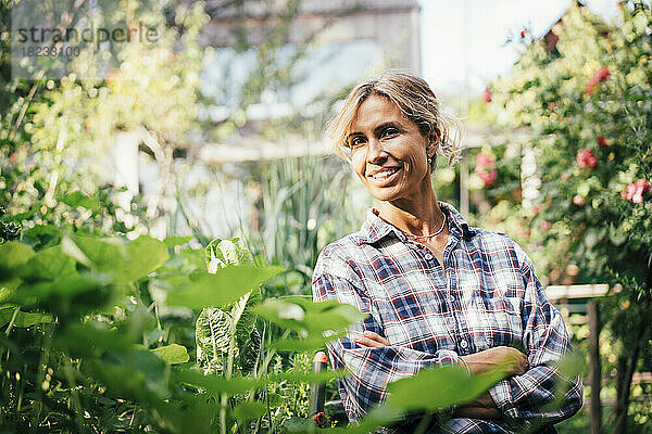 Reife Frau lächelt mit verschränkten Armen im Gemüsegarten