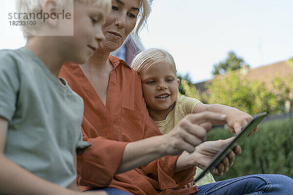 Frau sitzt mit Kindern am Tablet-PC
