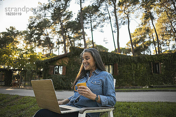 Lächelnde reife Frau  die draußen mit Laptop sitzt