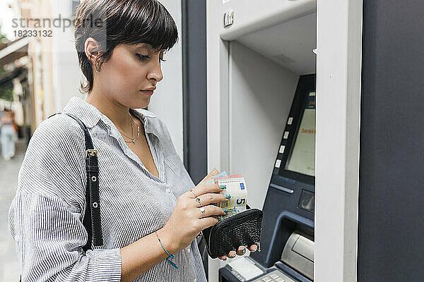 Junge Frau zählt Geld aus der Handtasche am Geldautomaten