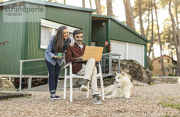 Smiling mature couple with dog and laptop outside green building
