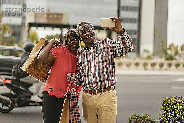 Mann macht Selfie mit Smartphone  Frau hält Einkaufstüten in der Hand