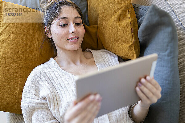 Lächelnde junge Frau entspannt sich und nutzt den Tablet-PC zu Hause