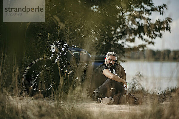 Nachdenklicher reifer Mann sitzt vor dem Motorrad