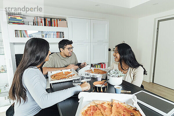 Glückliche Frauen und Männer essen Pizza am Esstisch im Wohnzimmer