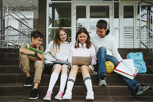 Mädchen macht Hausaufgaben über Laptop von Freunden  die auf Stufen in der Schule sitzen