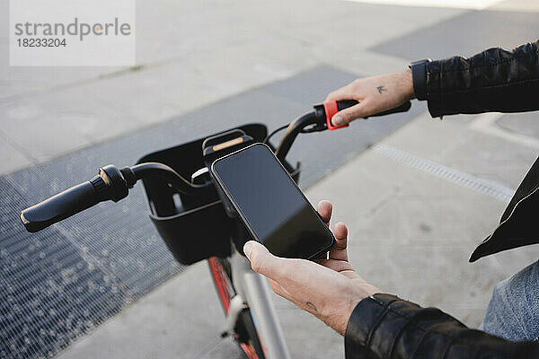 Hand eines Mannes  der auf dem Fußweg ein Fahrrad per Mobiltelefon mietet
