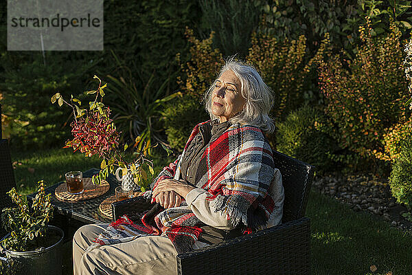 Ältere Frau sitzt im Herbstgarten in einem Sessel
