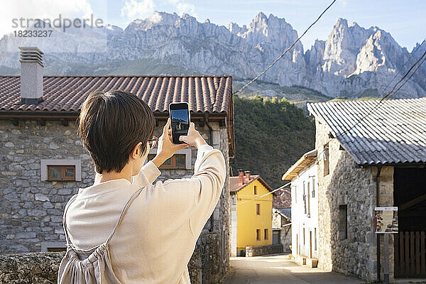 Spain  Castile and Leon  Posada de Valdeon  Female tourist taking photos of stone houses in Picos de Europa