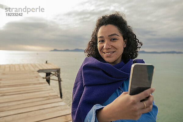 Frau mit Smartphone macht Selfie am Steg am Meer