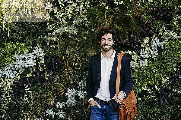 Lächelnder Geschäftsmann mit der Hand in der Tasche  der vor Pflanzen steht
