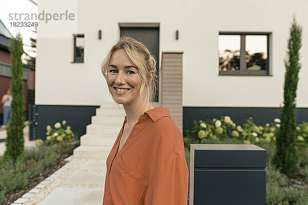 Lächelnde Frau mit blonden Haaren vor dem Haus