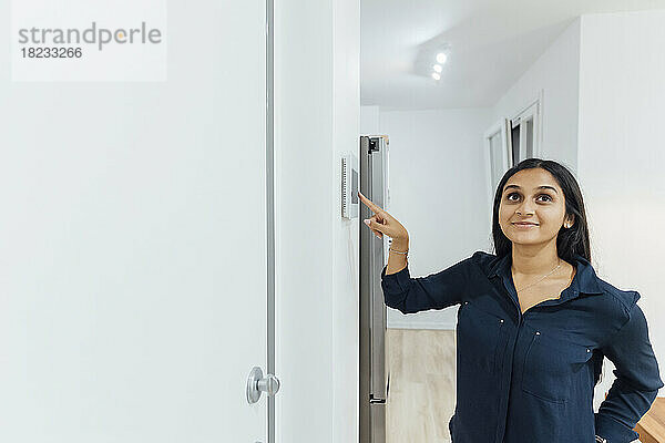 Lächelnde junge Frau benutzt Smart-Home-Gerät an der Wand
