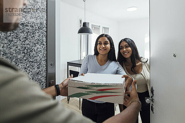 Lächelnde junge Frauen erhalten Pizza vom Zusteller