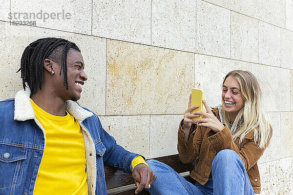 Glückliche Frau fotografiert Freund über Smartphone an der Wand